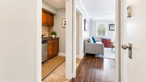 Un pasillo que da a una cocina con armarios de madera y un comedor con sofá y cortinas.