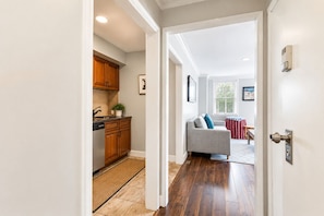 A hallway leading to a kitchen with wooden cabinets and a dining area with a sofa and curtains. - Downtown Atlanta 1BR Condo on 24th Floor with Balcony, Walk to Stadium (Atlanta)