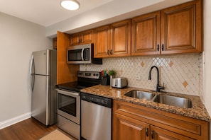 A kitchen with wooden cabinets, stainless steel appliances, a granite countertop, and a patterned backsplash. - Downtown Atlanta 1BR Condo on 24th Floor with Balcony, Walk to Stadium (Atlanta)