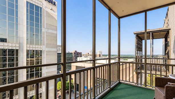 Un balcón con vistas a un paisaje urbano, un edificio con el letrero 'LABER' y una silla de mimbre.