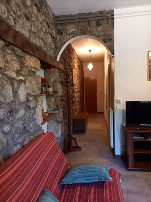 Ein gemütliches Zimmer mit Steinwand, einer hölzernen Bank, einem Fernseher und einem Flur, der in ein weiteres Zimmer führt.