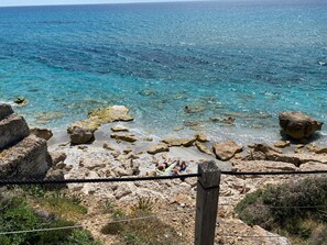 Paisaje costero con mar azul cristalino, terreno rocoso y una valla de madera.