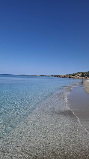 A beach with clear water, pebbly shore, and rocky cliffs in the background. - Cottage in the countryside a few kilometers from the beaches of the Sinis Peninsula (Sardegna)