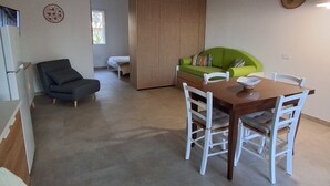 Et spiseområde med et træbord, hvide stole, en grøn sofa og en dekorativ panel.