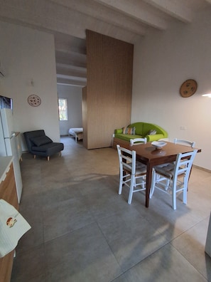 Un coin repas avec une table en bois et des chaises blanches, un canapé vert et un panneau décoratif.