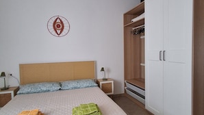Et soveværelse med seng, garderobe, vægdekoration og et natbord.