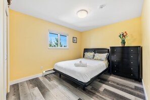 Un dormitorio con cama, cómoda, ventana y un florero con flores.