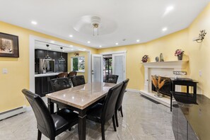 Un comedor con una mesa de mármol y sillas negras, una cocina con armarios negros y una chimenea con adornos decorativos.