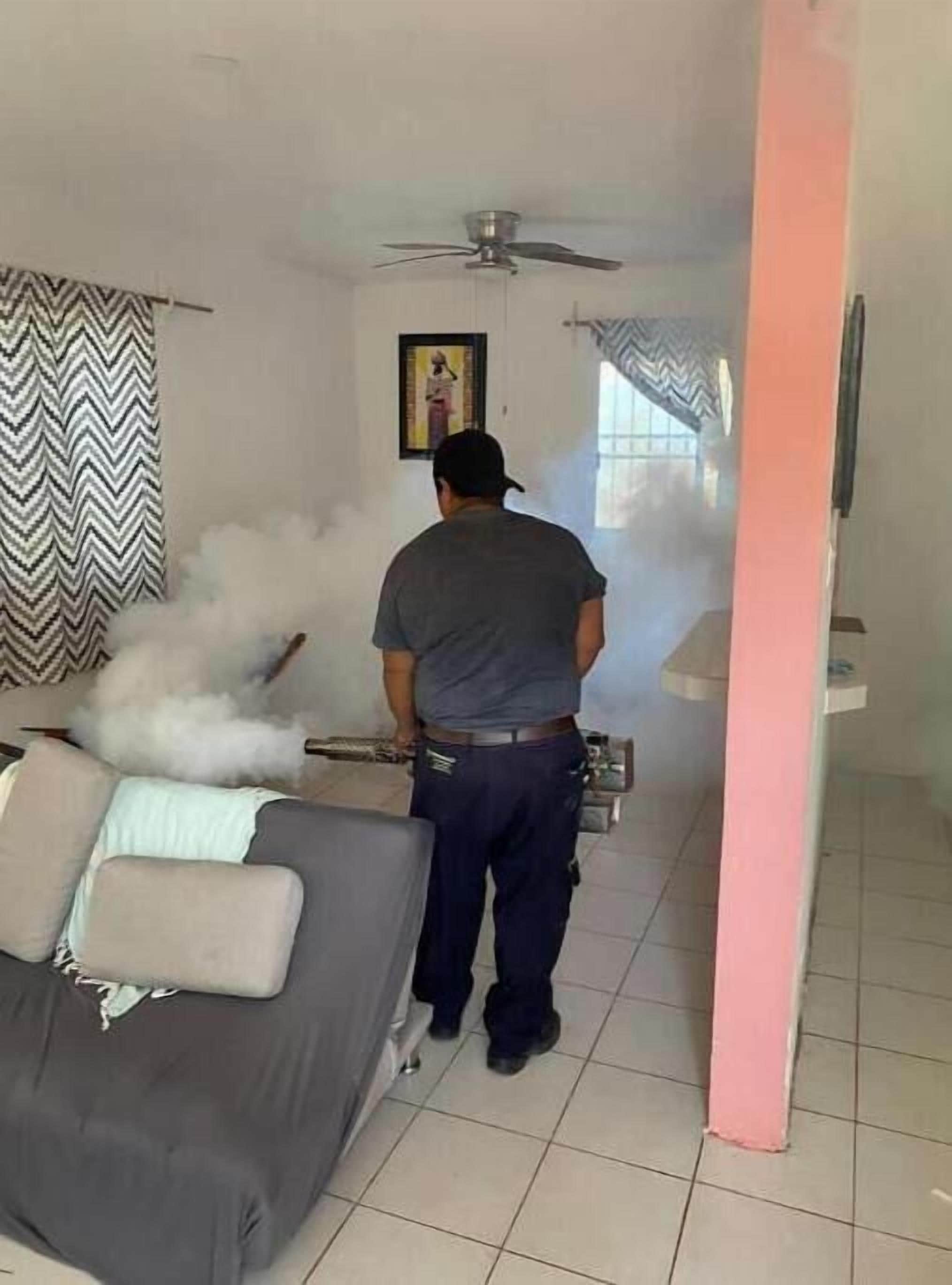Una persona de pie en una habitación con un ventilador de techo, un sofá y un pilar rosa.