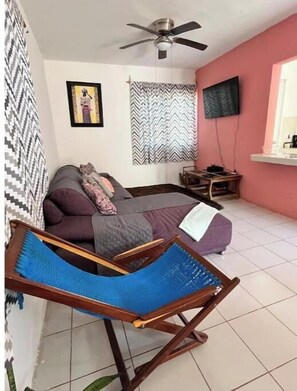 Ein Zimmer mit einem Bett, einem blauen Hängesessel, einem Deckenventilator, einem Fernseher und einer Wand mit Muster.