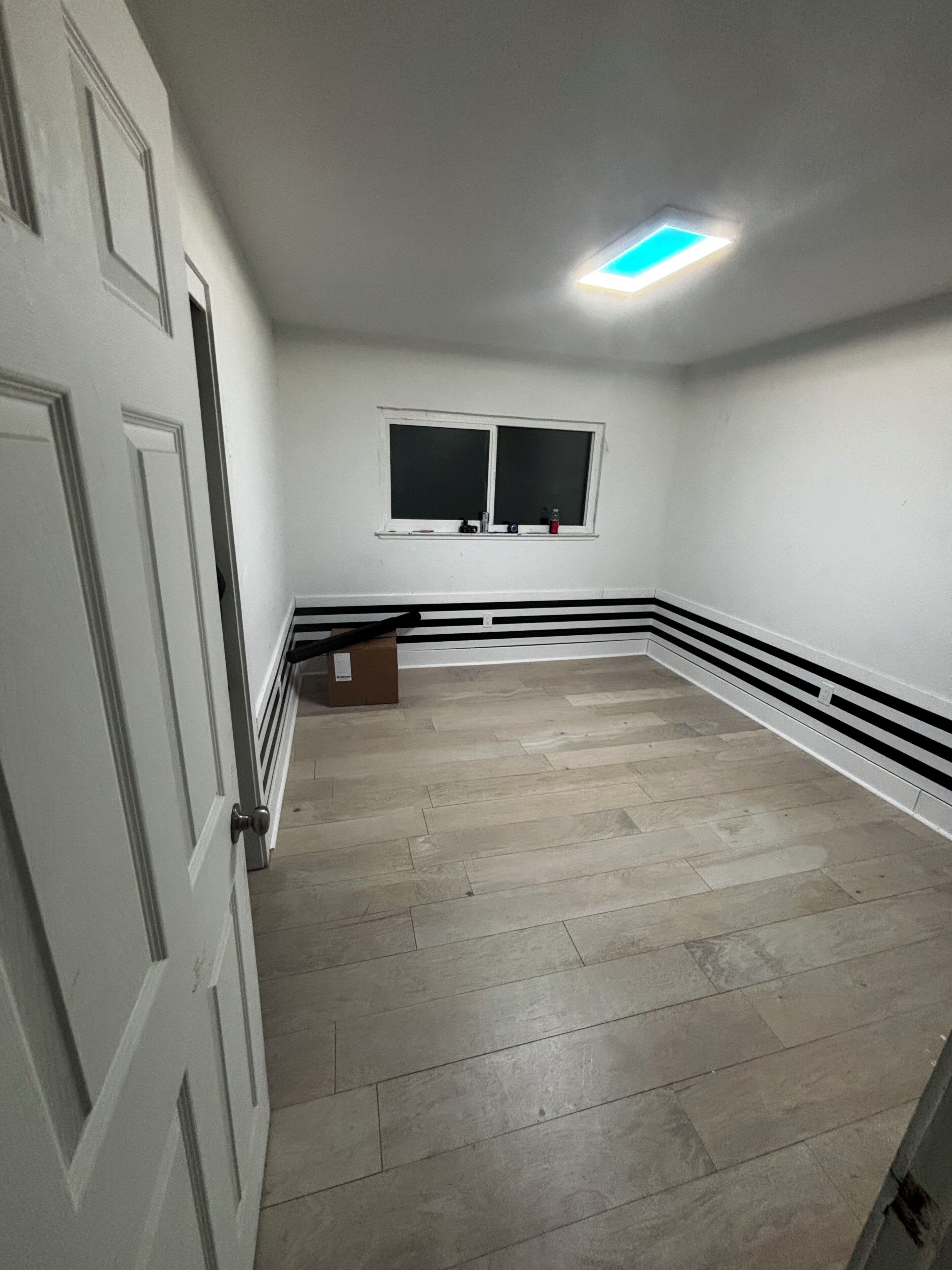 A room with a white door, a window, and a ceiling light.