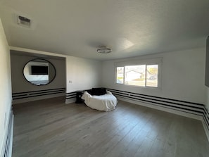 Una habitación con un ventanal grande, un espejo redondo y una cama.