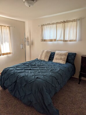 A bedroom with a bed, a nightstand, a floor lamp, and a window with curtains.