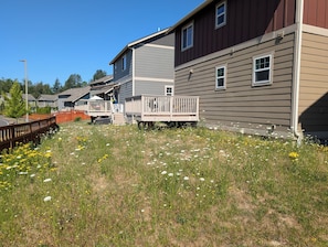 A residential area with houses, a wooden deck, and a grassy field with wildflowers.