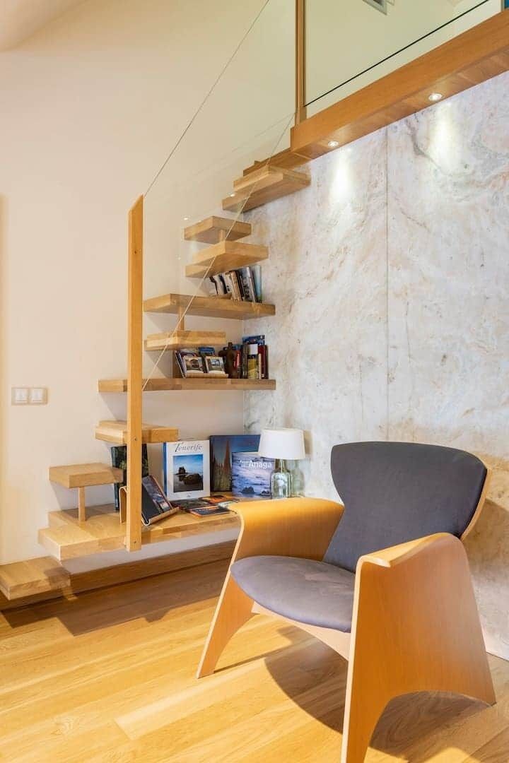 A modern interior with a wooden staircase, a grey armchair, and a marble wall.