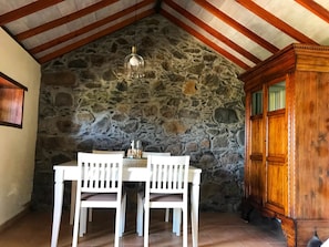 Ein Essbereich mit Steinsandsteinwand, Holzbalkendecke, einem Tisch mit Stühlen und einem Holzschrank.
