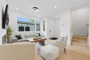 Una sala de estar moderna con sofá, sillón, mesa de centro y televisor montado en la pared.