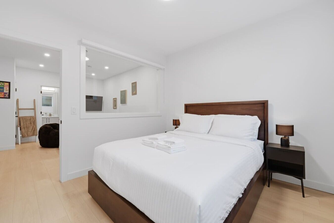 A bedroom with a large bed, a nightstand, a bedside lamp, a mirror, and a door leading to another room.