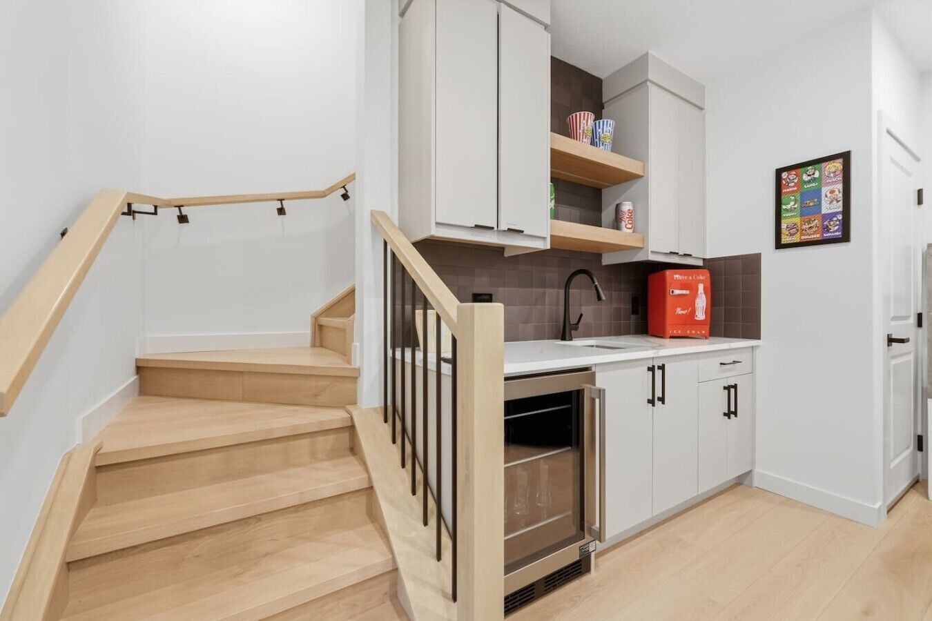 A modern kitchen with wooden stairs, a built-in oven, and a red appliance on the countertop.