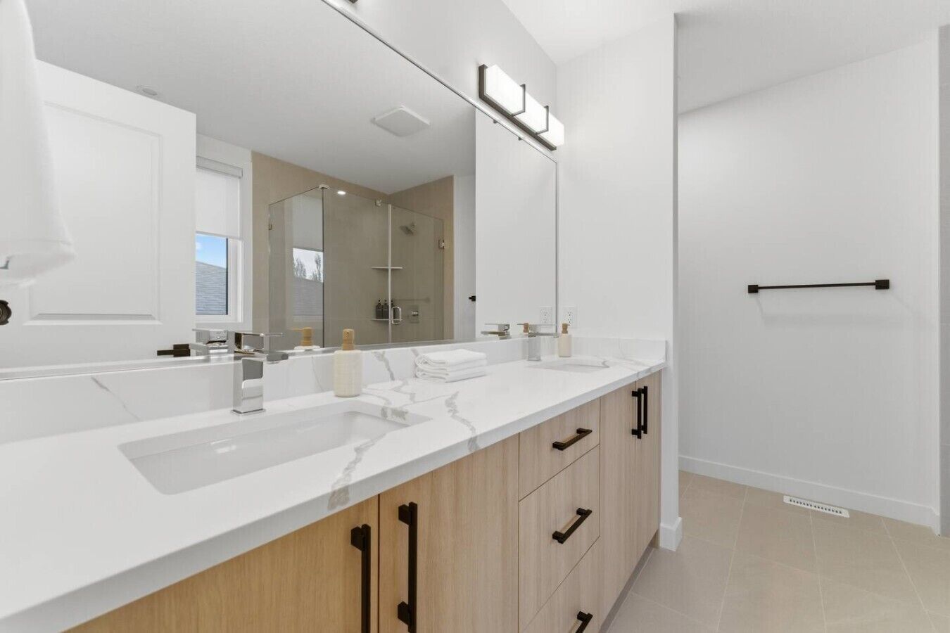 Een moderne badkamer met een grote spiegel, twee wastafels en een douche.