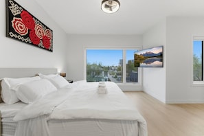 Camera da letto moderna con un ampio letto, vista sulla città attraverso una finestra e un quadro appeso al muro.