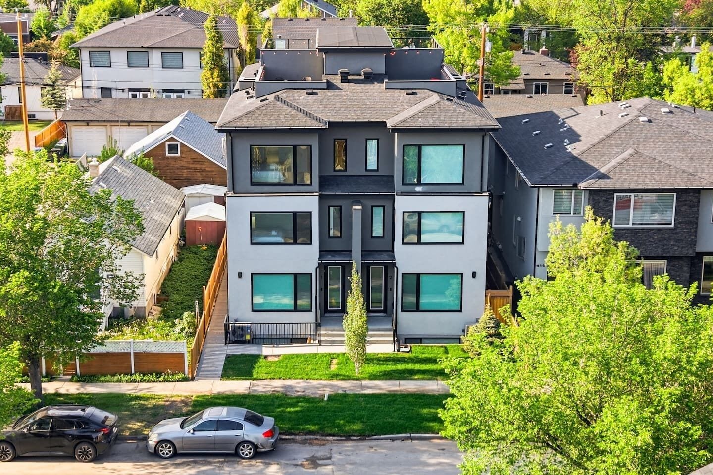 A modern two-story residential building with a flat roof, large windows, and a visible garage.