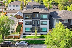 A modern two-story residential building with a flat roof, large windows, and a visible garage.