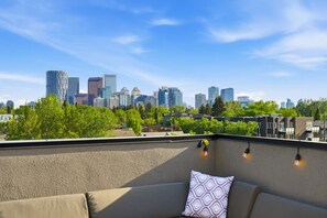 En tagterrasse med udsigt over byens skyline, en sofa og lyskæder.