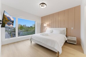 A modern bedroom with a large window, a bed, a bedside table, and a wall-mounted light fixture.