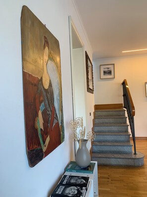 A staircase with a wooden handrail and a white wall with a large abstract painting and a framed picture. - Villa top view Lake Como (Faggeto Lario)