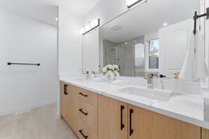 A modern bathroom with a large mirror, two sinks, and wooden cabinets. - Spacious Calgary Home | Rooftop Views | Sleeps 10 (Calgary)
