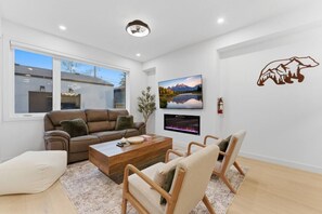 Un salon moderne avec un canapé, une table basse et des fauteuils, une cheminée et une grande fenêtre.