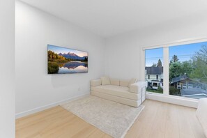 A modern living room with a large window, a beige sofa, and a framed landscape painting. - Spacious Calgary Home | Rooftop Views | Sleeps 10 (Calgary)