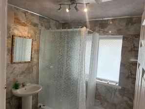 Ein Badezimmer mit Dusche, Waschbecken, Spiegel und Fenster.