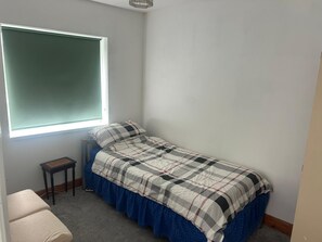Ein kleines Zimmer mit Einzelbett, Fenster, Tisch und Stuhl.