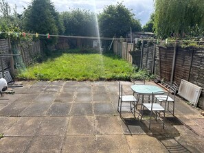 Eine Terrasse mit Tisch und Stühlen, ein Rasen und ein Holzzaun.