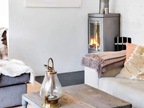 A cozy living room with a fireplace, a sofa, a coffee table with a lantern, and a wall-mounted shelf. - 4 Star Holiday Home in Dronningmolle (Dronningmolle)