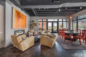 Un salon moderne doté d’une cheminée, de sièges confortables, d’un coin repas avec des chaises rouges et de grandes fenêtres offrant une vue sur la ville.