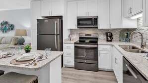 Una cocina moderna con armarios blancos, electrodomésticos de acero inoxidable, encimera de granito y una isla central con zona de comedor.