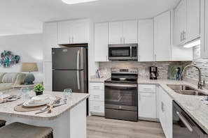 A modern kitchen with white cabinets, stainless steel appliances, a granite countertop, and a central island with dining setup. - Ocean Forest Villas B112 (Myrtle Beach)