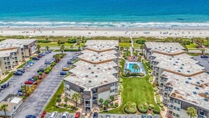 Un hotel frente a la playa con varias edificaciones, estacionamiento y zona de piscina.