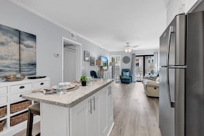 A modern kitchen with a central island, a dining area with a sofa, and a view to the outside. - Ocean Forest Villas B112 (Myrtle Beach)