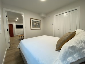Ein Schlafzimmer mit Bett, einem Gemälde an der Wand, einer Tür und einem Gang zu einem weiteren Raum.