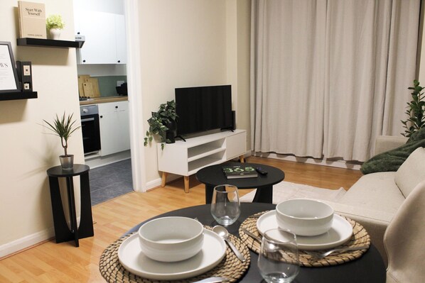 Uma sala de estar moderna com televisão de tela plana, sofá, mesa de centro e área de jantar com pratos e tigelas.