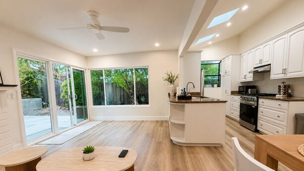 A modern kitchen with white cabinets, a central island, and a dining area with a round table and chairs. -  4BR Near UCSB & Santa Barbara • Private Hot Tub • Walk to Beach • Pool access (Goleta)