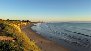 A beach with a curved shoreline, grassy dunes, and a clear sky. -  4BR Near UCSB & Santa Barbara • Private Hot Tub • Walk to Beach • Pool access (Goleta)