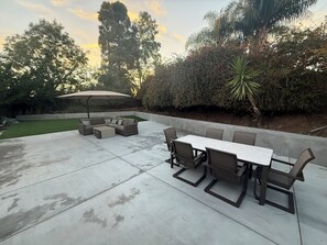 A patio with a sectional sofa, a dining table with chairs, and an umbrella.