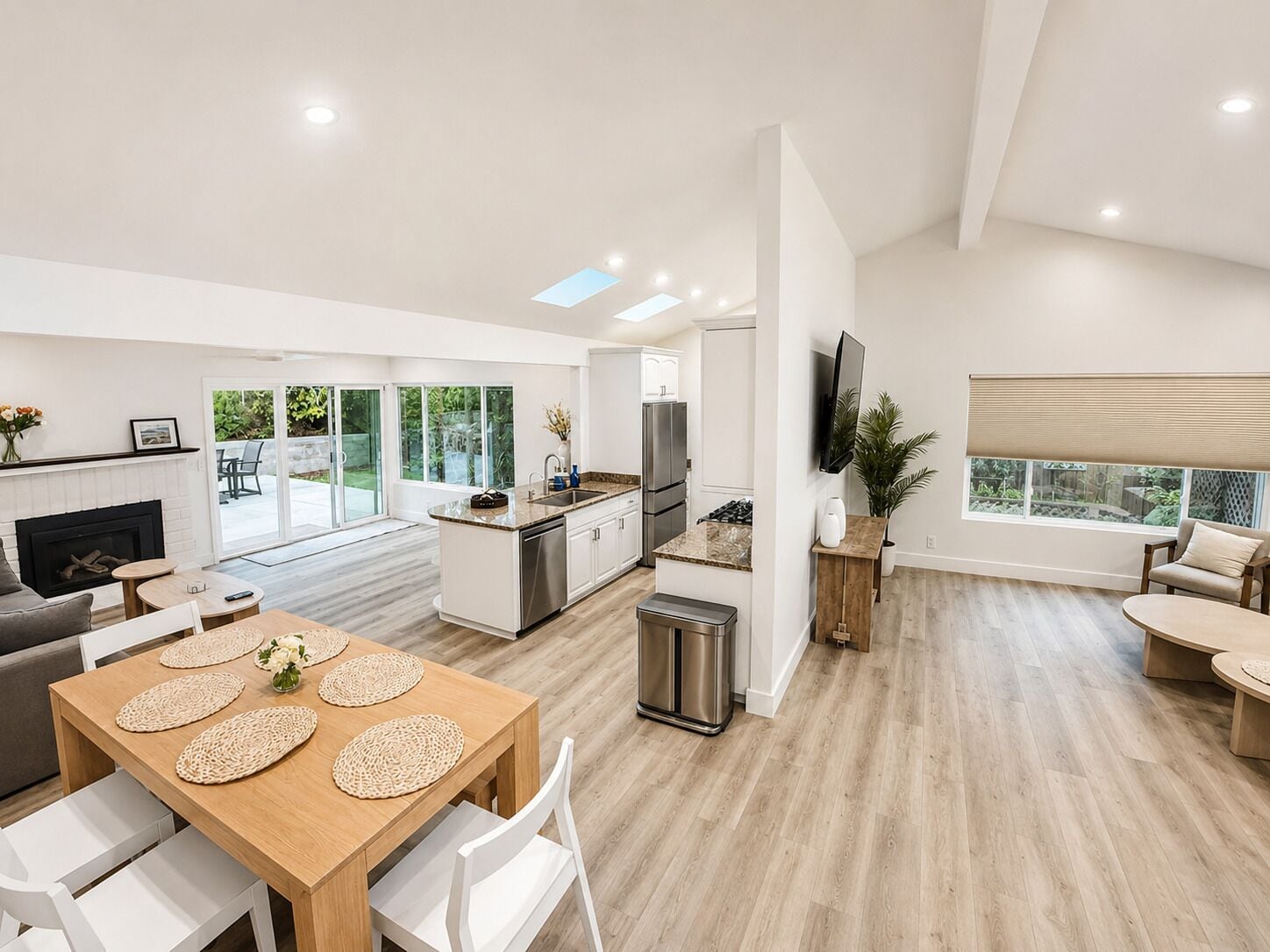 A modern kitchen with a central island, a dining area with a wooden table, and a living room with a sofa and a TV.