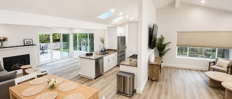 A modern kitchen with a central island, a dining area with a wooden table, and a living room with a sofa and a TV.