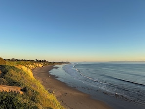 A beach with a curved shoreline, grassy dunes, and a clear sky.